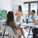 Asian woman lead young group of multiethnic businesspeople in team meeting, using laptop computer for ESG topic presentation on monitor.