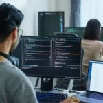 software developers working on multiple screens displaying code and application diagrams in a modern office
