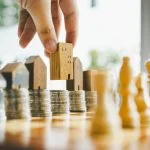 Chess, stack of coins and house models in chess game, competition success play. strategy, management or leadership