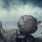 Business man pushing large stone up to hill